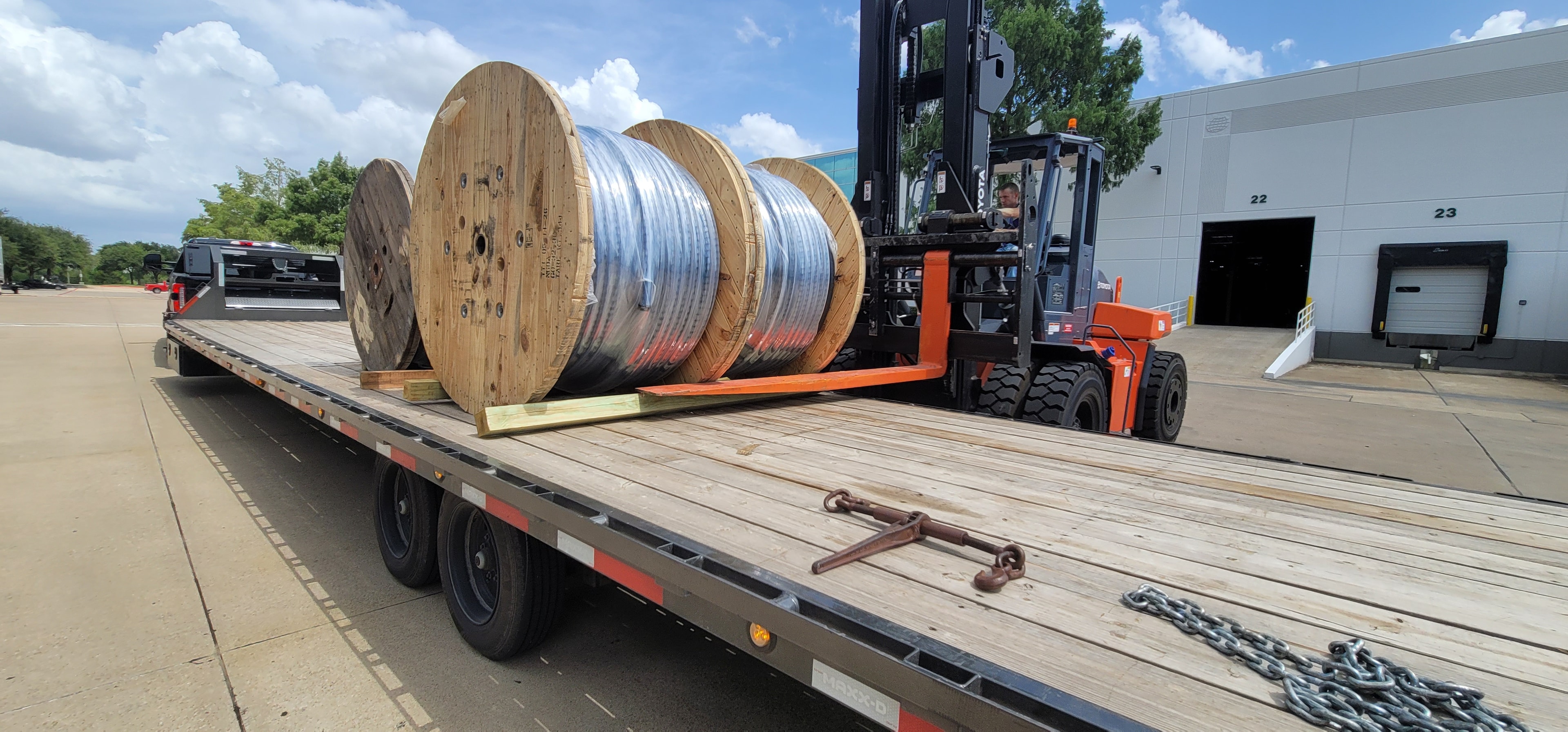 Forklift loading large cable spools onto flatbed trailer